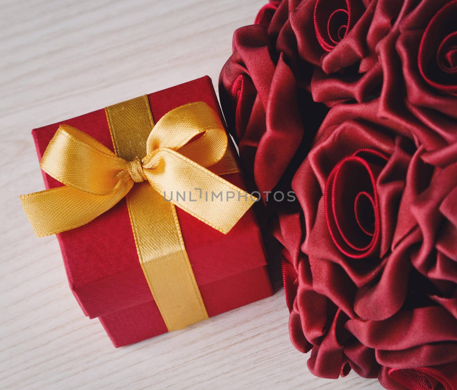 red roses and red gift box with yellow ribbon on wooden surface