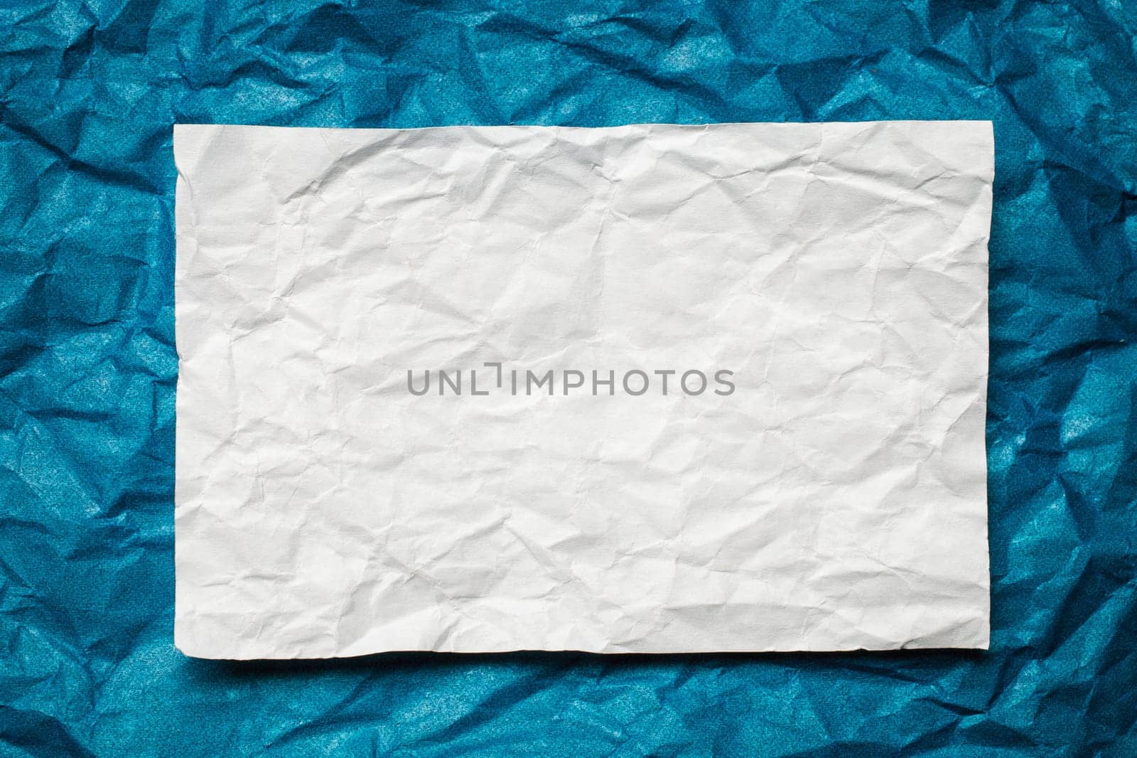 Crumpled  white paper card on blue background, place for tex