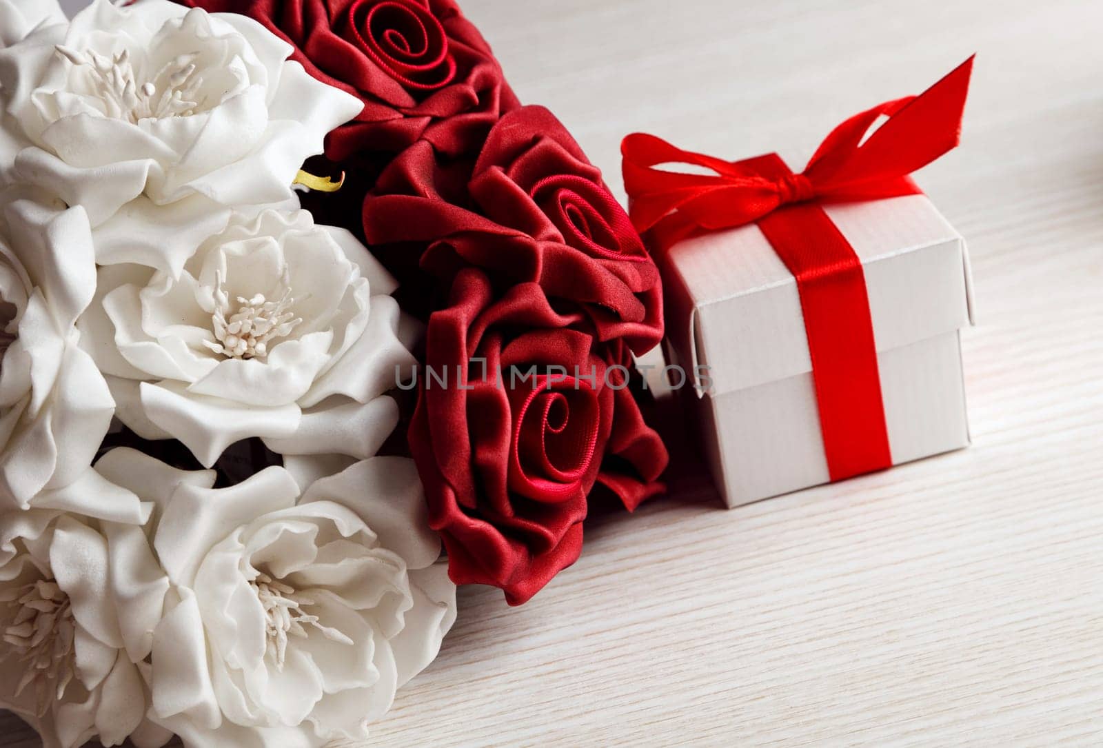 red and white roses and red gift box with yellow ribbon on wooden surface