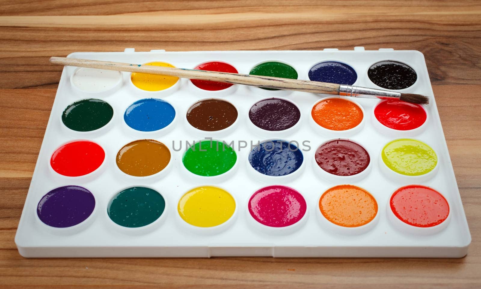 Colorful Aquarelle paints in a box and brushes on  wooden background