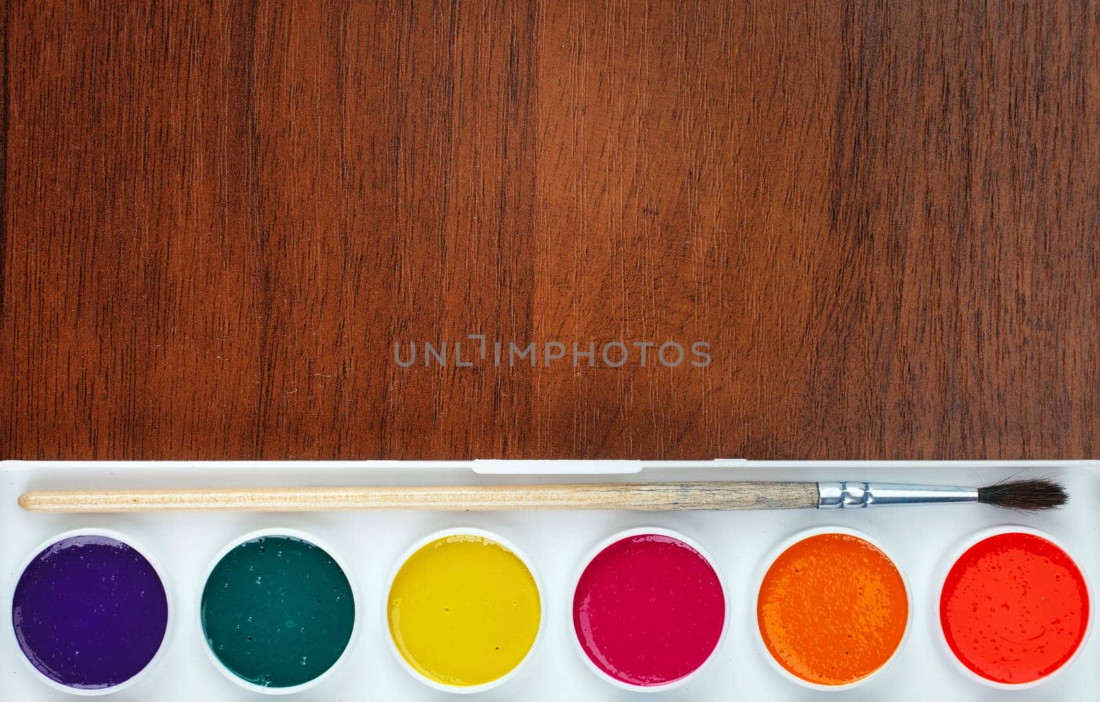 Colorful Aquarelle paints in a box and brushes on wooden background, place for text