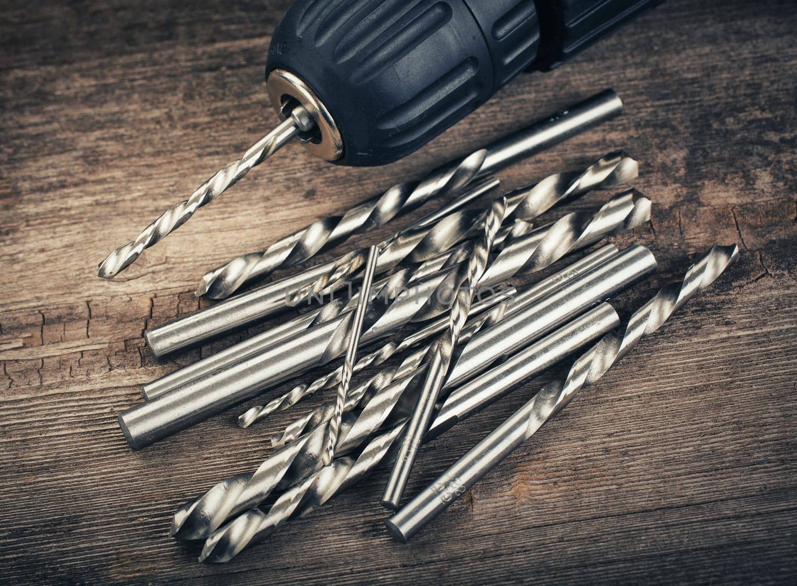 Drill and set of drill bits with screws on wooden background