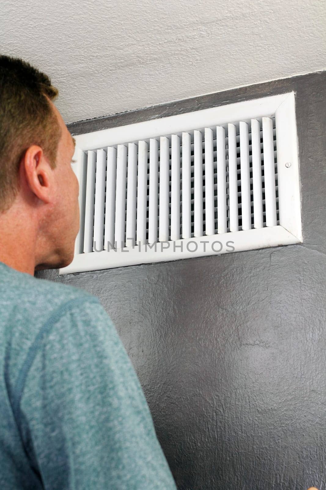Male examines an indoor air duct register for dirt to understand if he should get it cleaned. One guy in his forties peers into and inspects a furnace central heating vent..