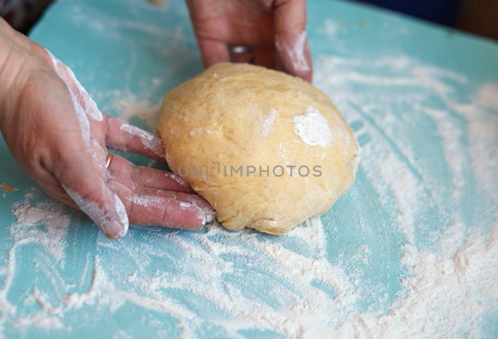 Woman's hands knead dough on a blue table