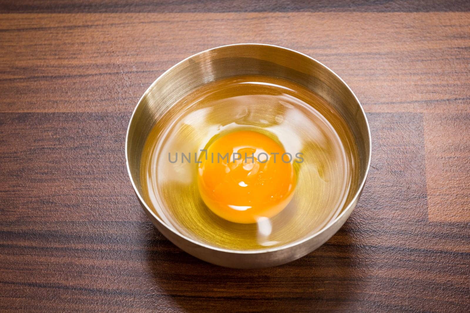 One egg: egg yolks and egg whites in a bowl on a brown worktop