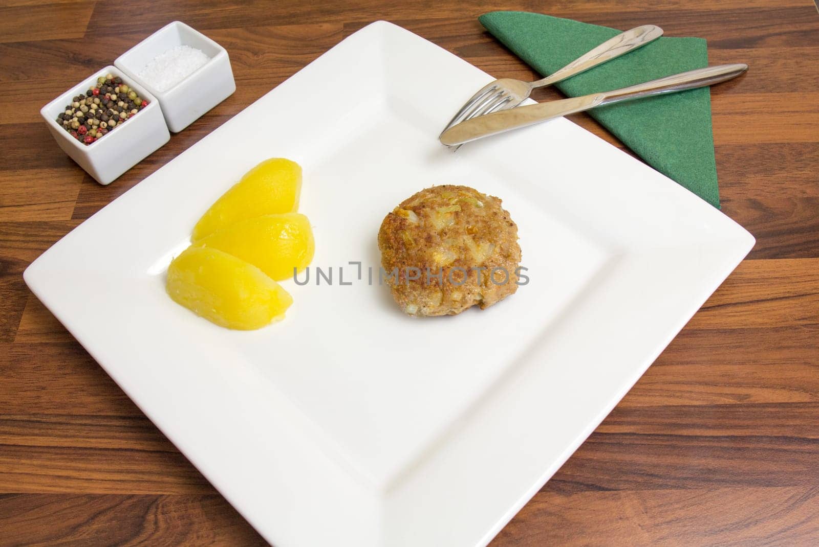 A freshly fried frikadell on a white plate,with potatoes and cutlery