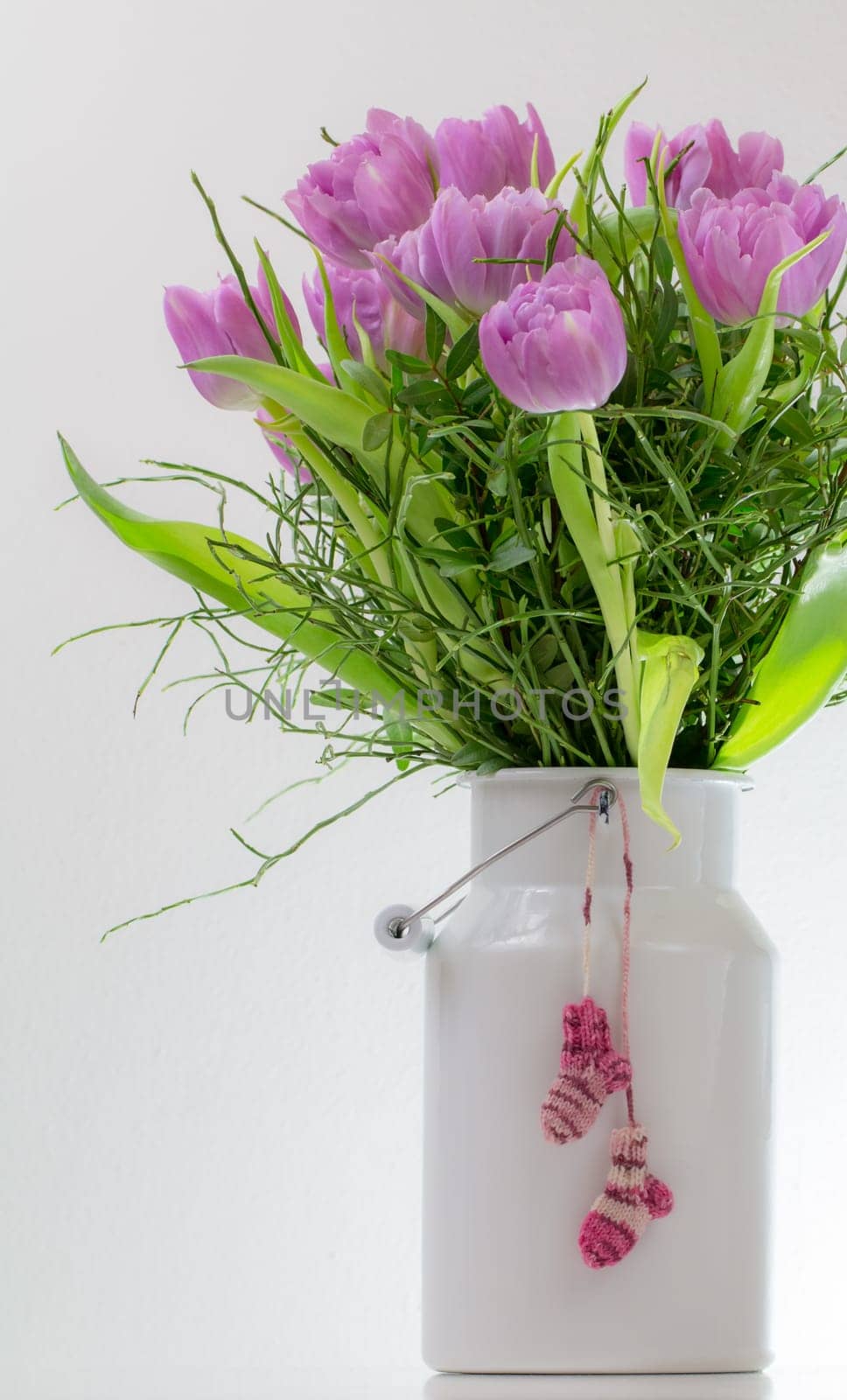 Baby socks hang on a white milk jug in which a bouquet of tulips is stuck