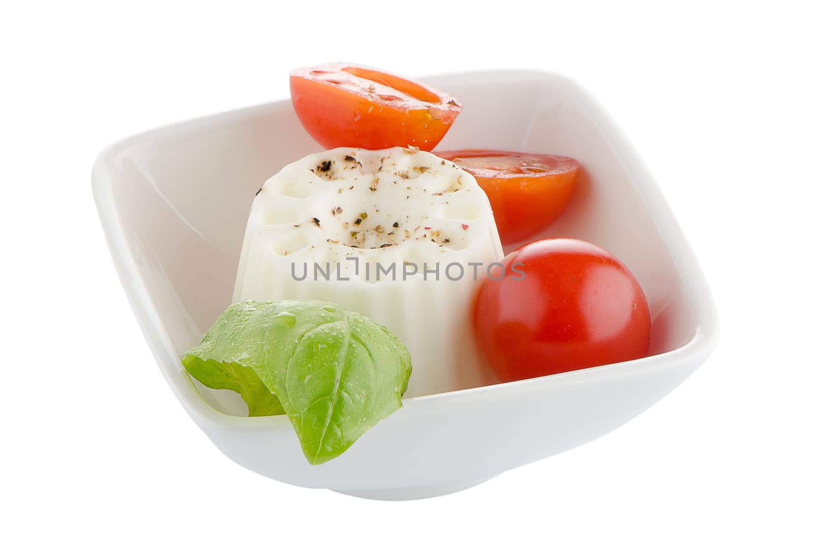 Fresh salad with goat cheese, tomato and basil pesto on a white cup.