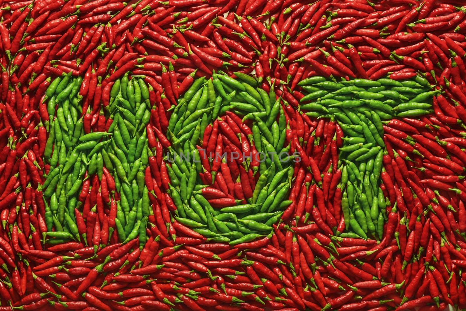 Word HOT written with green peppers, amid red peppers.
