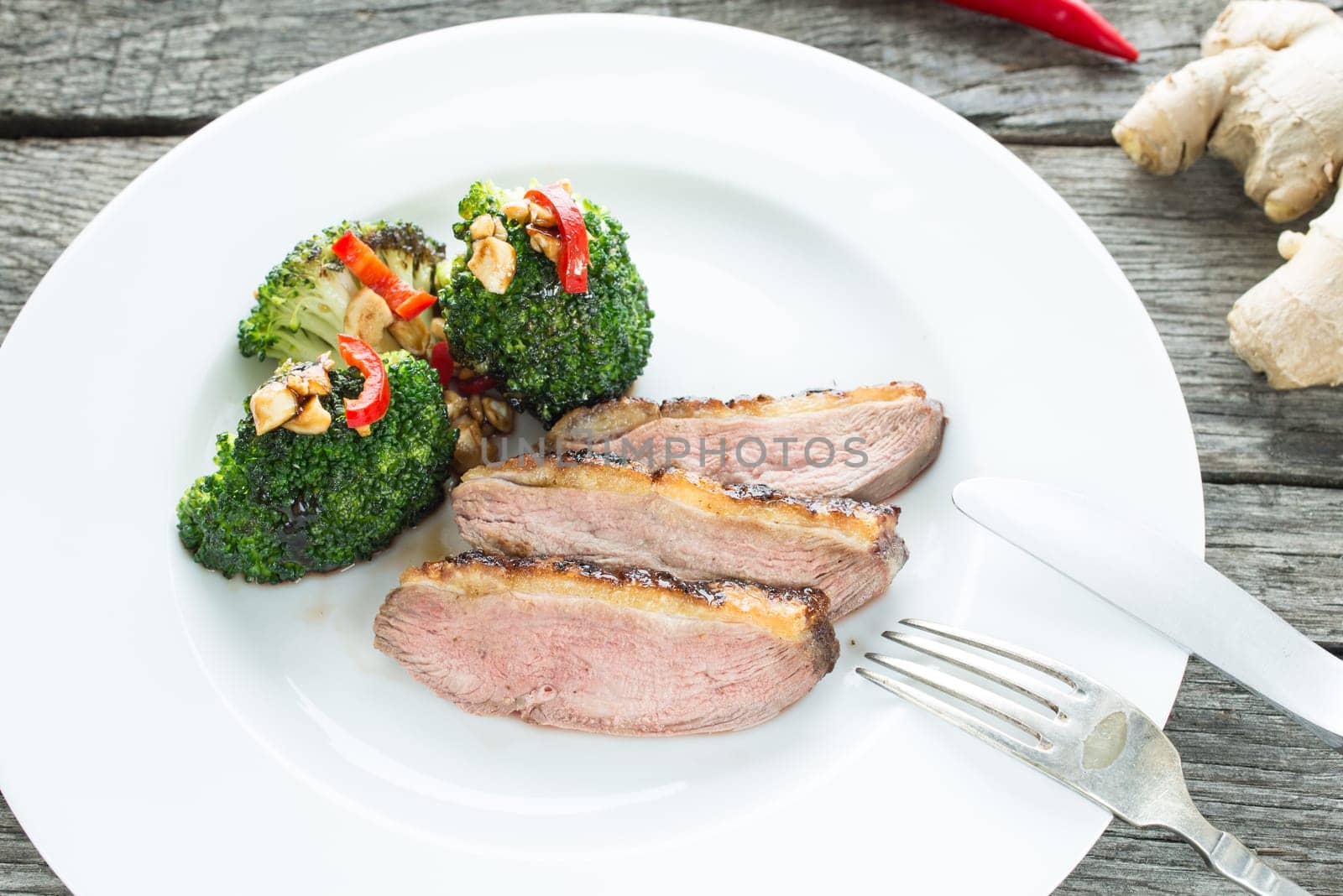 Slices of pink fried duck breast with broccoli