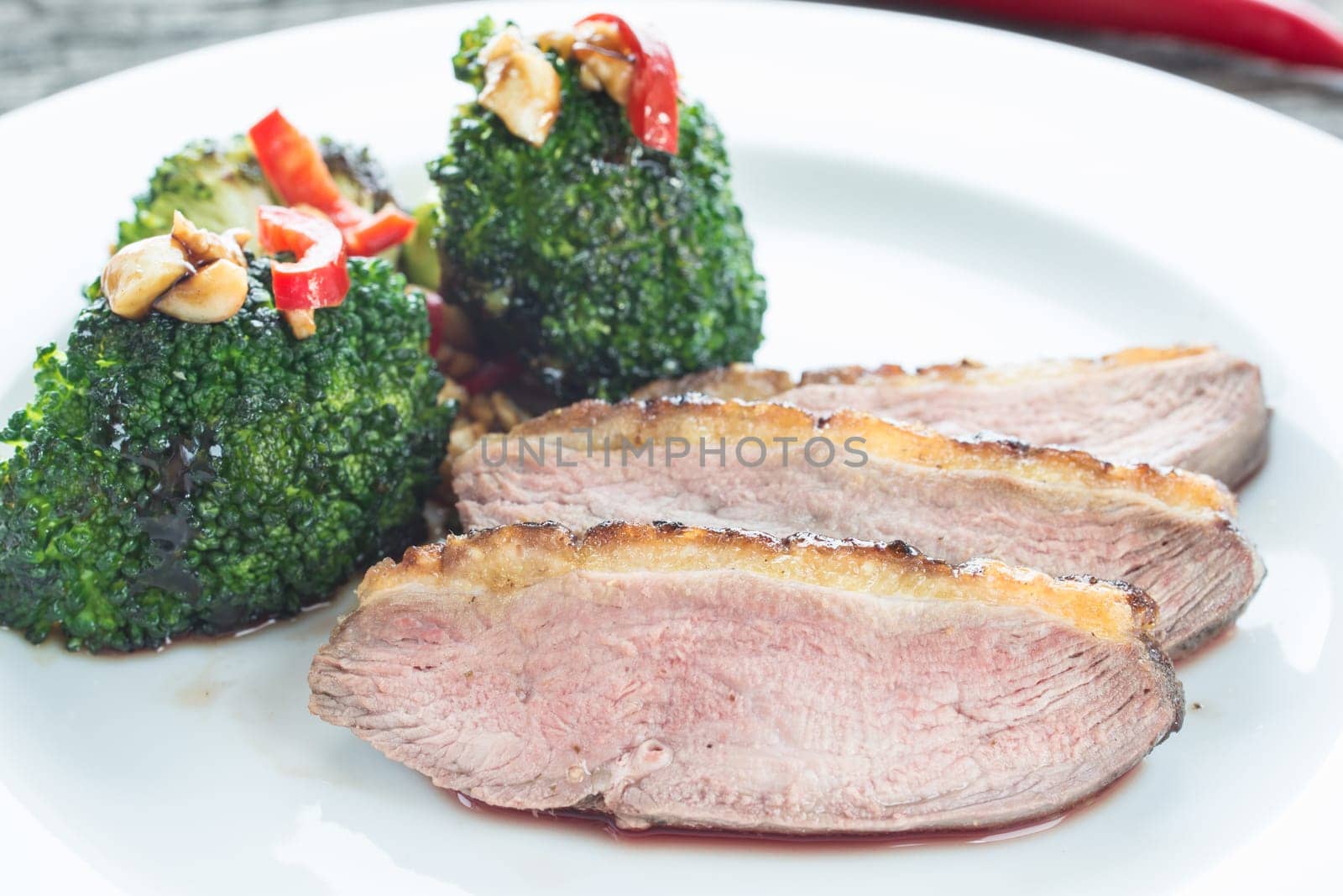 Slice of pink fried duck breast with broccoli and chilli
