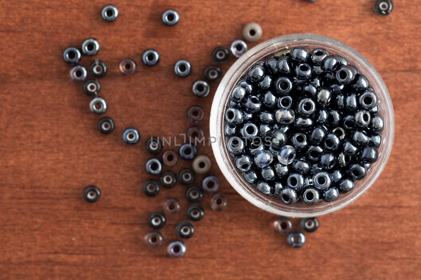 Shiny grey seed beads in a small container and on table, as seen from above.