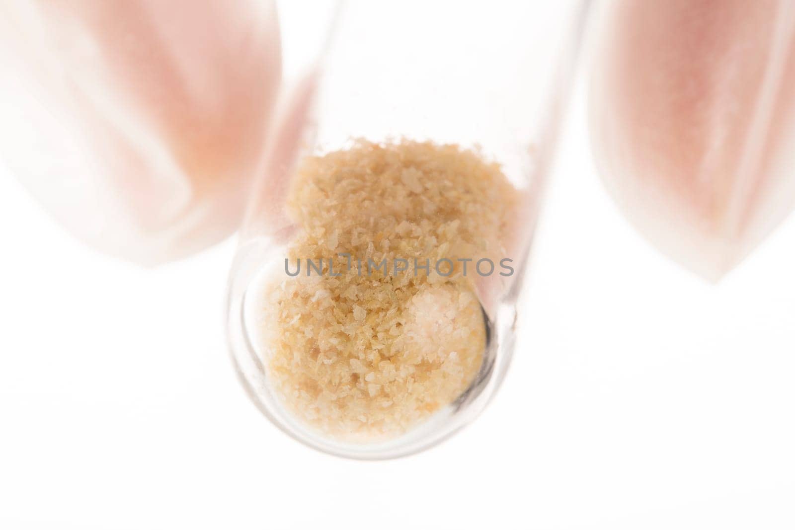 Brown crystals in test tube held by fingers on white background.