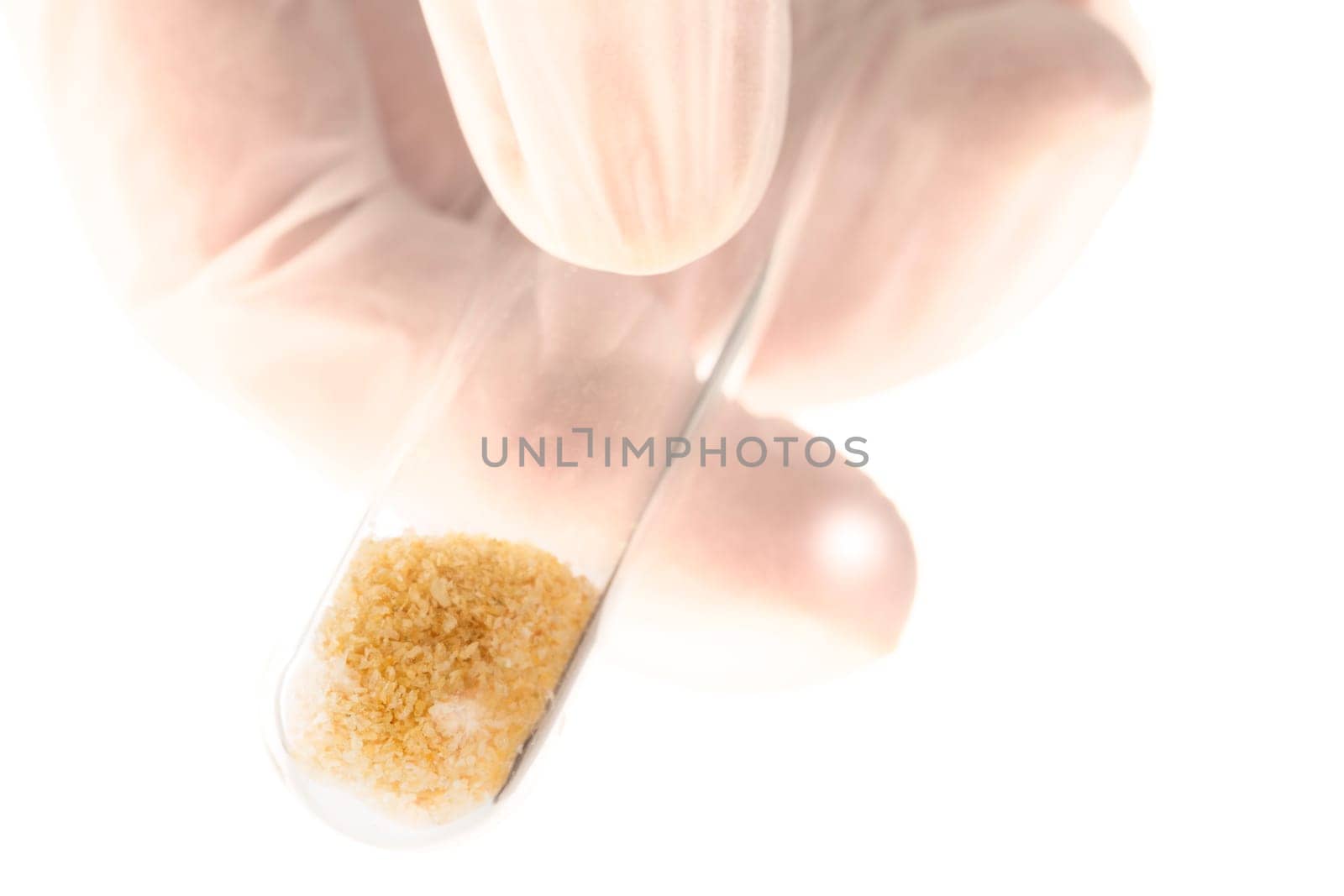Brown crystals in test tube held by fingers on white background.