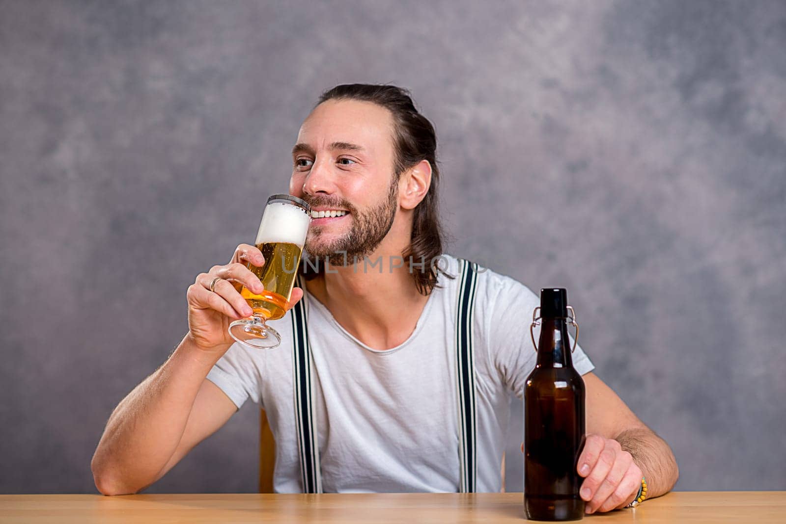 young man in front of gray background drinking beer