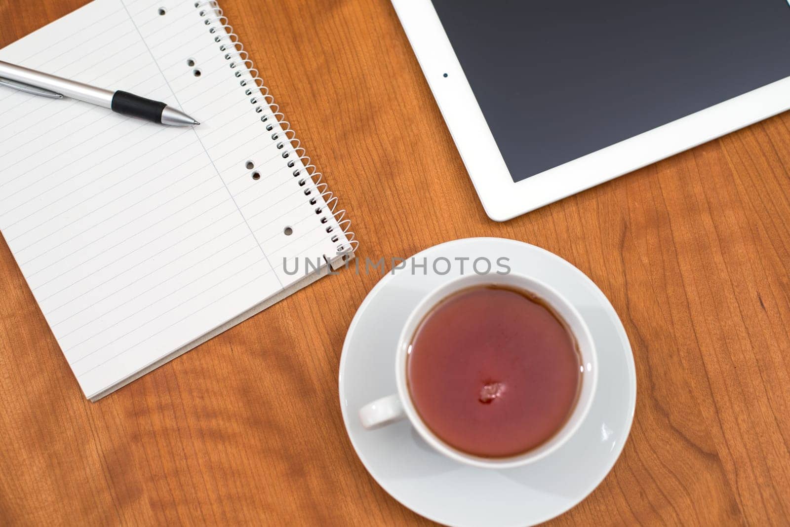 tablet PC, notepad with pen and a cup of tea on wooden table from above