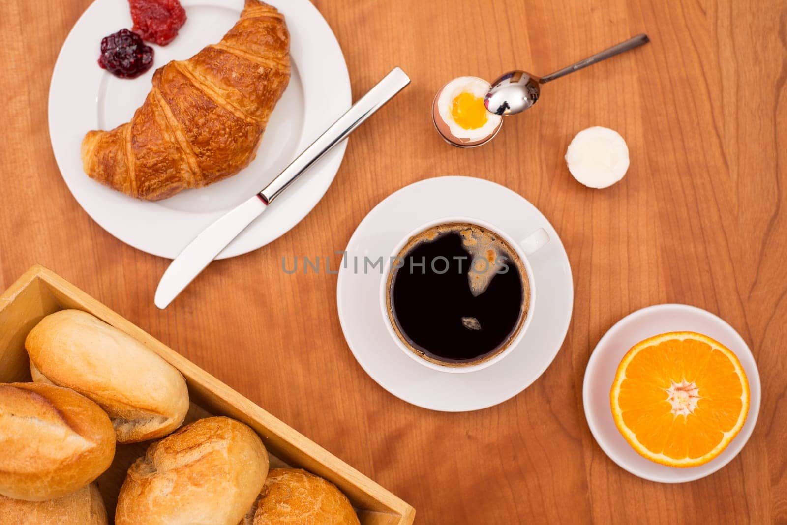 breakfast with croissant, bun, orange,coffee and egg on wooden table