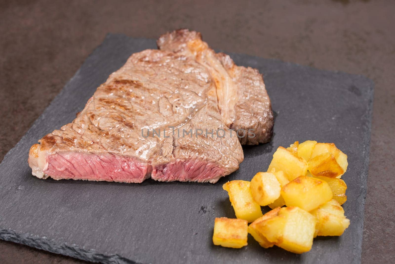 Pink fried dry aged rib eye steak with potatoes on