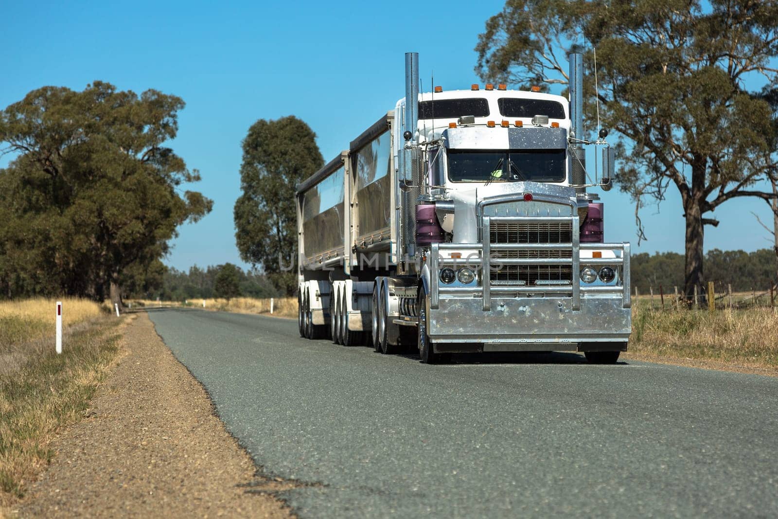 A large B-Double Semi Trailer driving down a deserted rural road.`