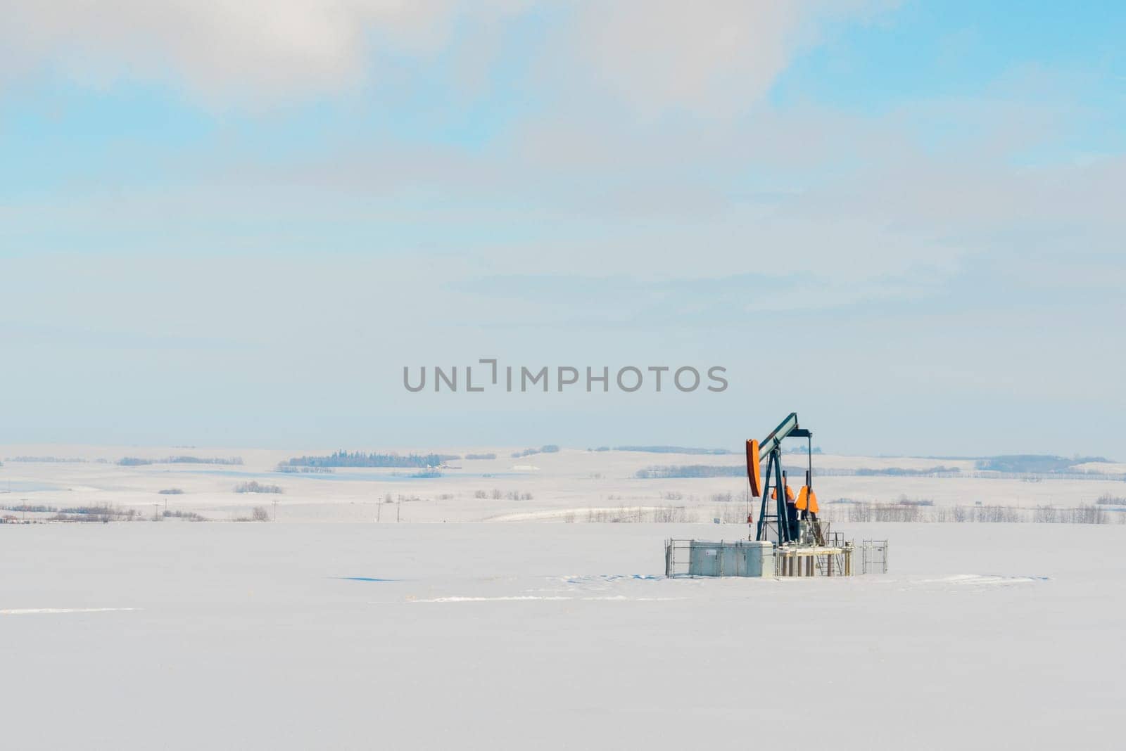 Landscape of a lone orange pumpjack in a snow covered field.