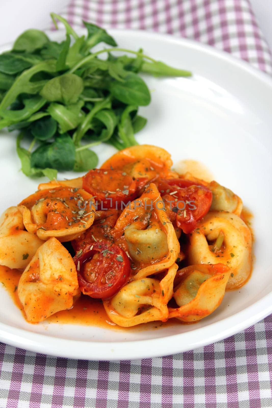 Tortellini with tomatoes in tomato and cream sauce and garnished with salad