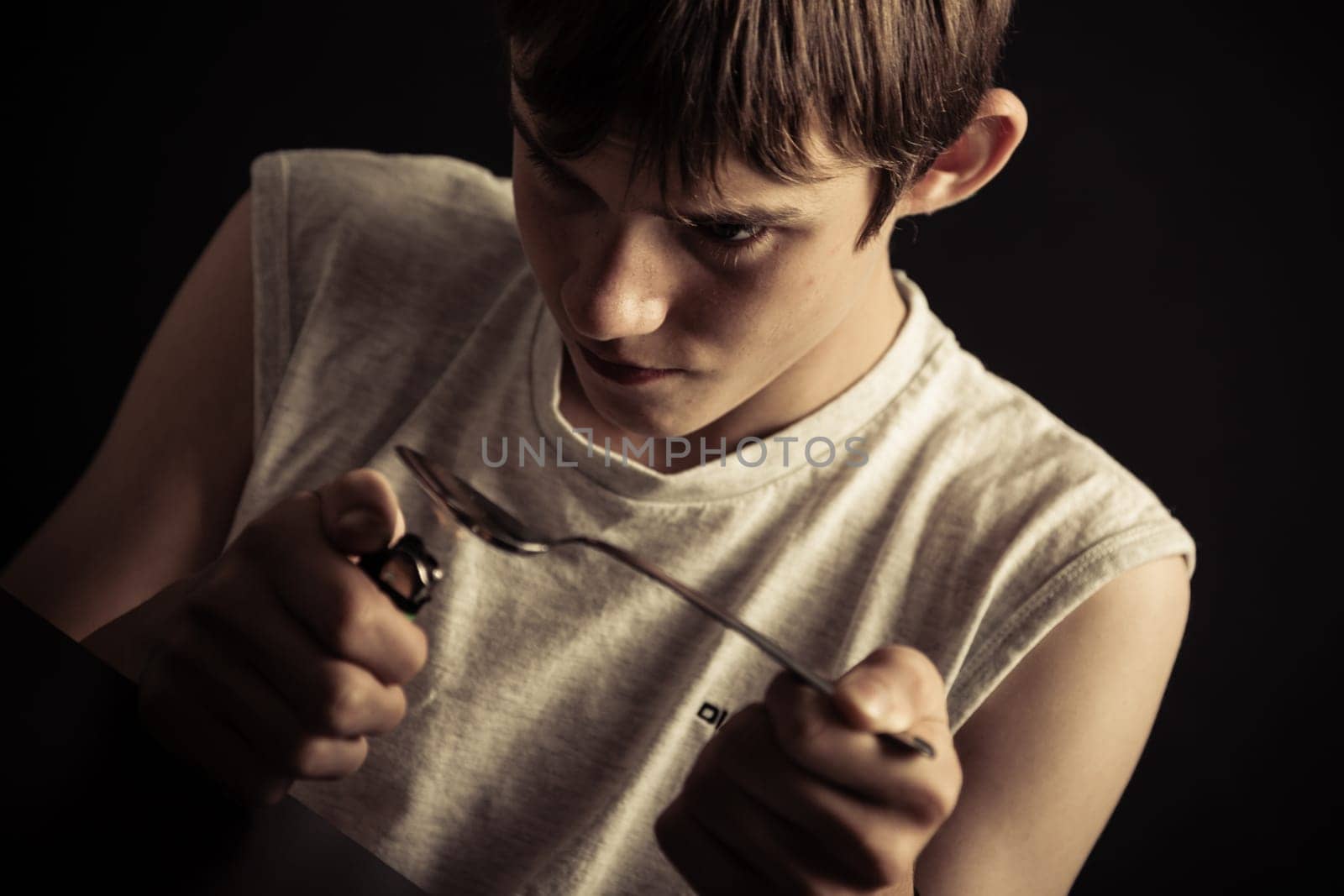 Single drug addicted sleeveless male teenager lighting spoon full of narcotics with cigarette lighter