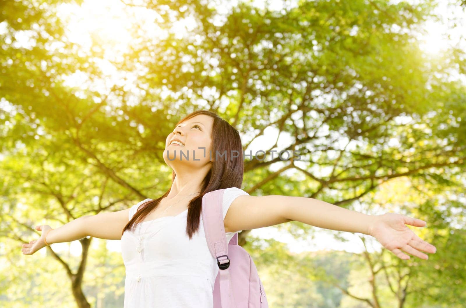 Young Asian college girl student standing on campus lawn, arms outstretched and smiling.