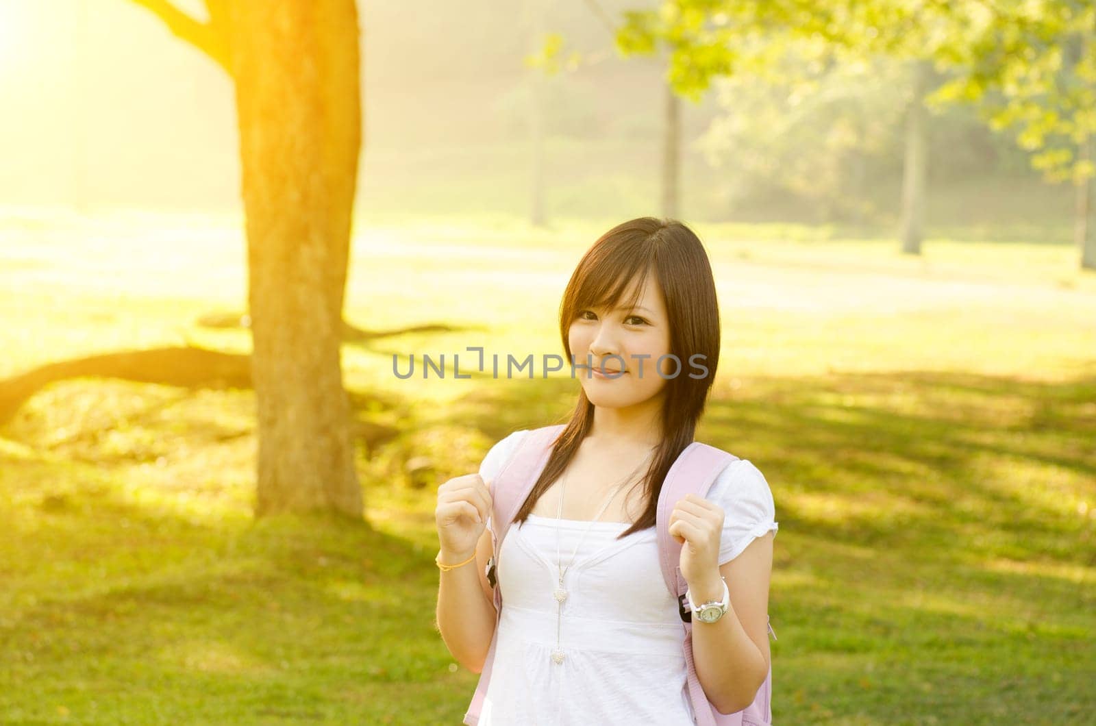 Young Asian college student standing on campus lawn, with backpack and smiling.