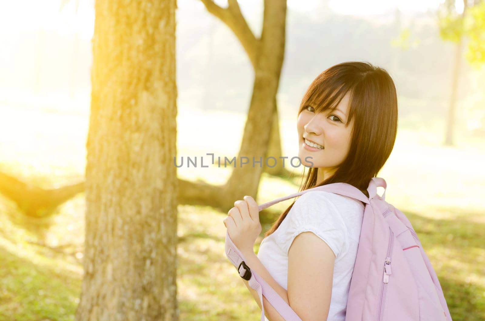 Young Asian university student standing on campus lawn, with backpack and smiling.