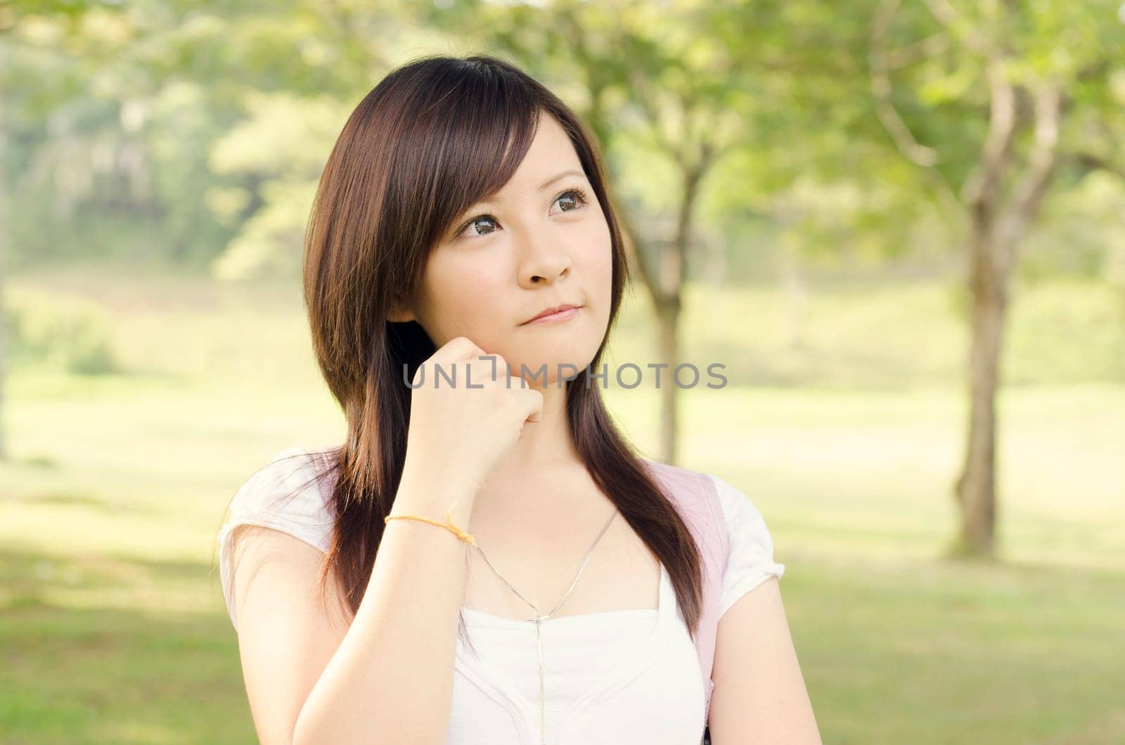 Young Asian college girl student standing on campus lawn, having a thought  and smiling.