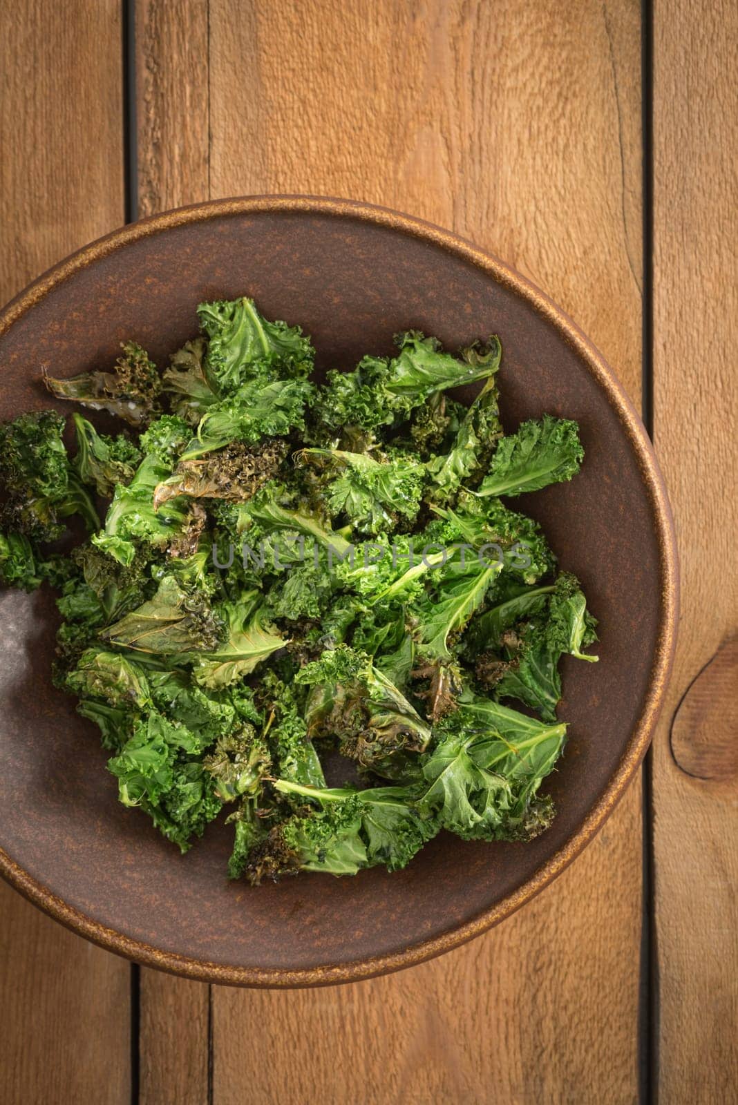 Kale chips with sea salt in a brown bowl on a wooden table