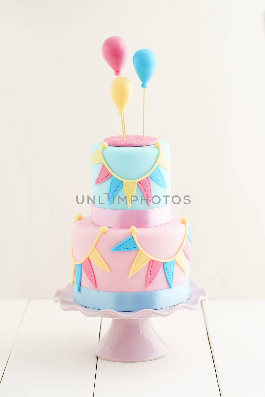 Fondant covered pastels coloured birthday cake with buntings and balloons