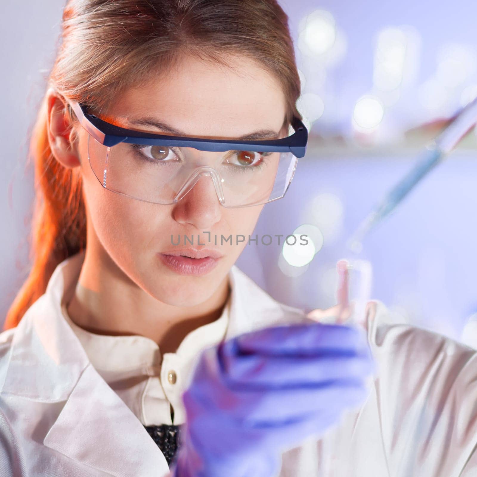 Life scientists researching in laboratory. Focused female life science professional pipetting solution into the glass cuvette. Lens focus on researcher&#39 s eyes. Healthcare and biotechnology concept.
