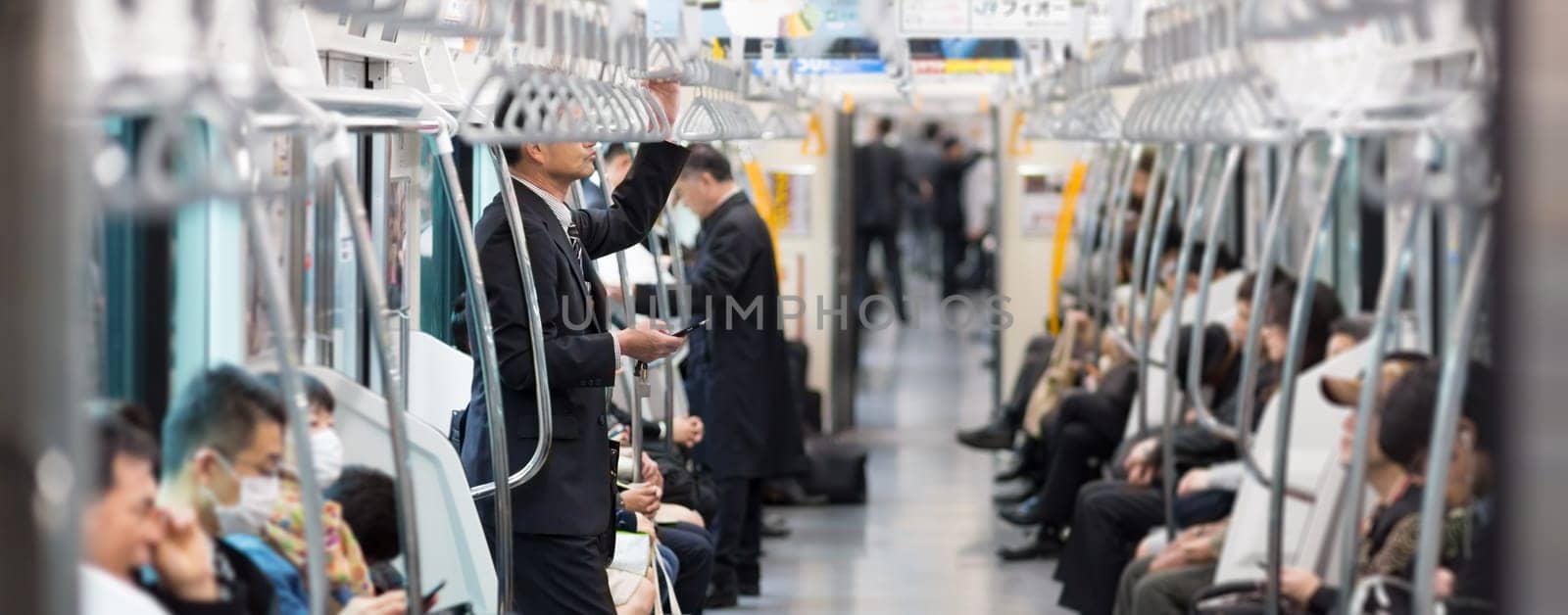 Passengers traveling by Tokyo metro. Business people commuting to work by public transport in rush hour. Shallow depth of field photo.