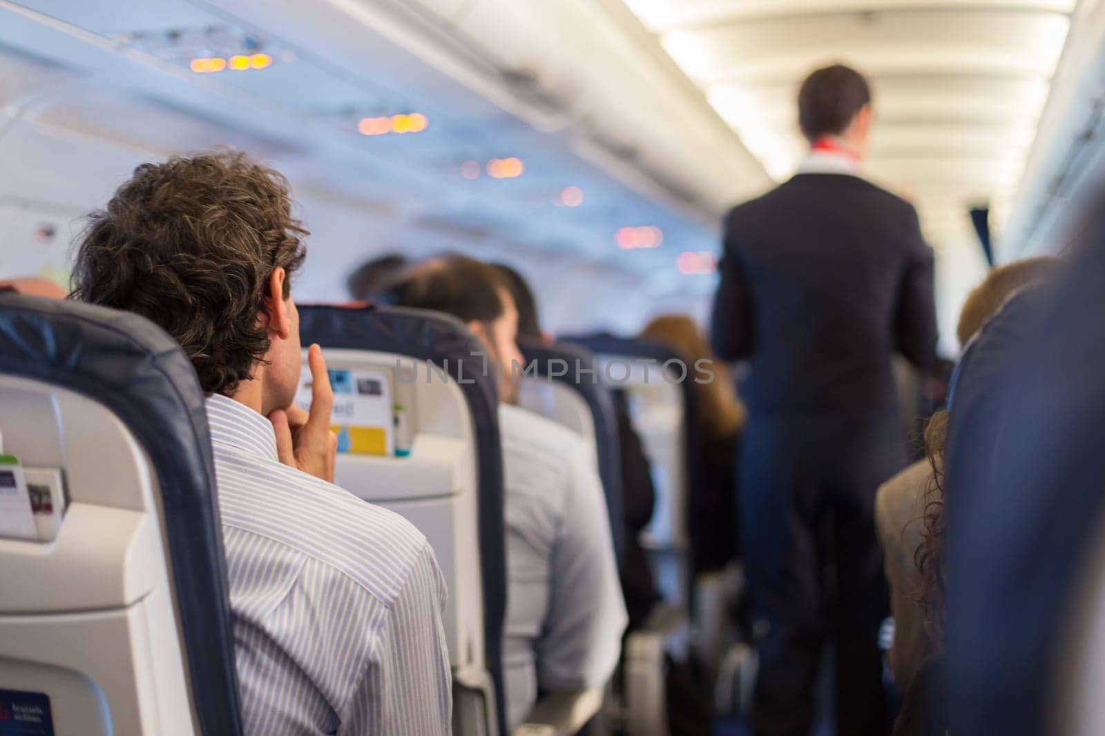 Interior of airplane with passengers on seats and steward walking the aisle.