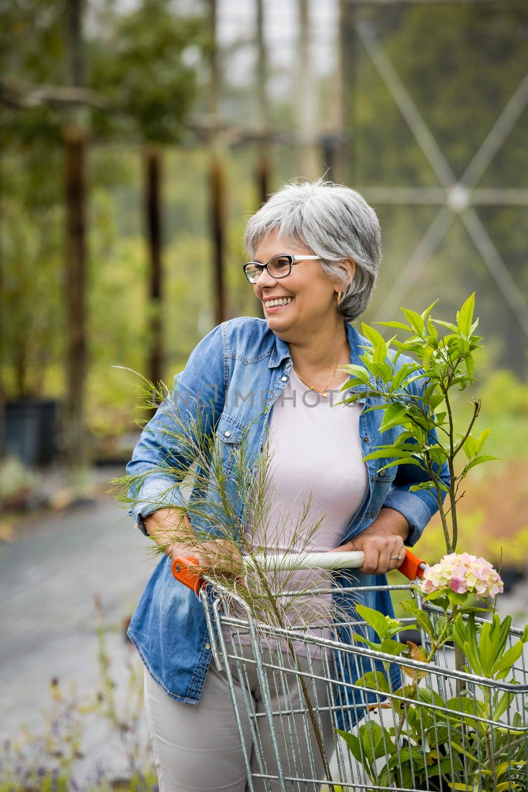 Beautiful mature woman working in a greenhouse holding flowers on her hands