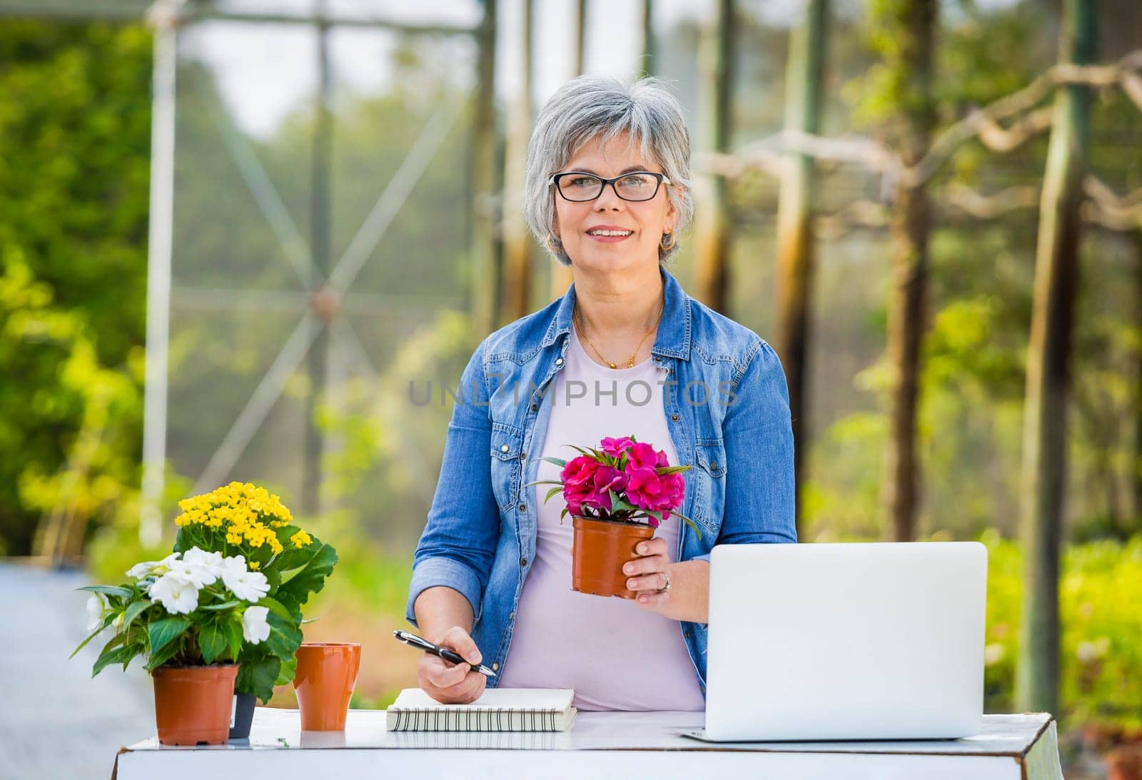 Beautiful mature woman working in a greenhouse holding flowers on her hands