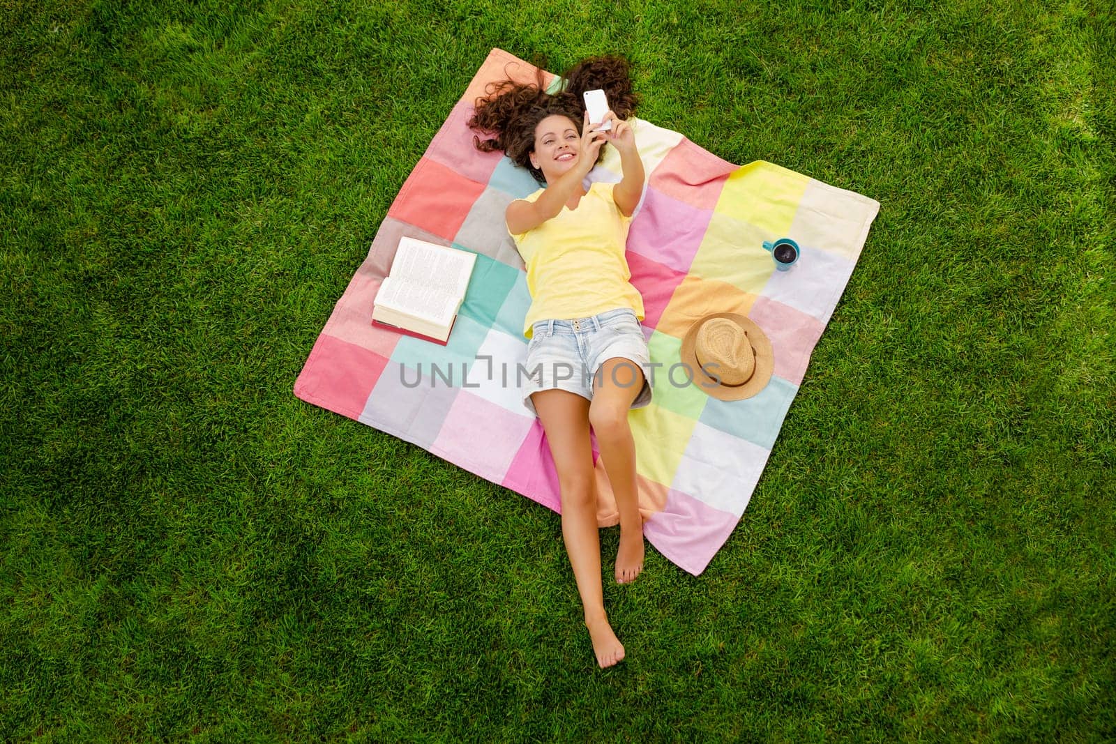 Smiling young woman lying on a blanket and making a selfie