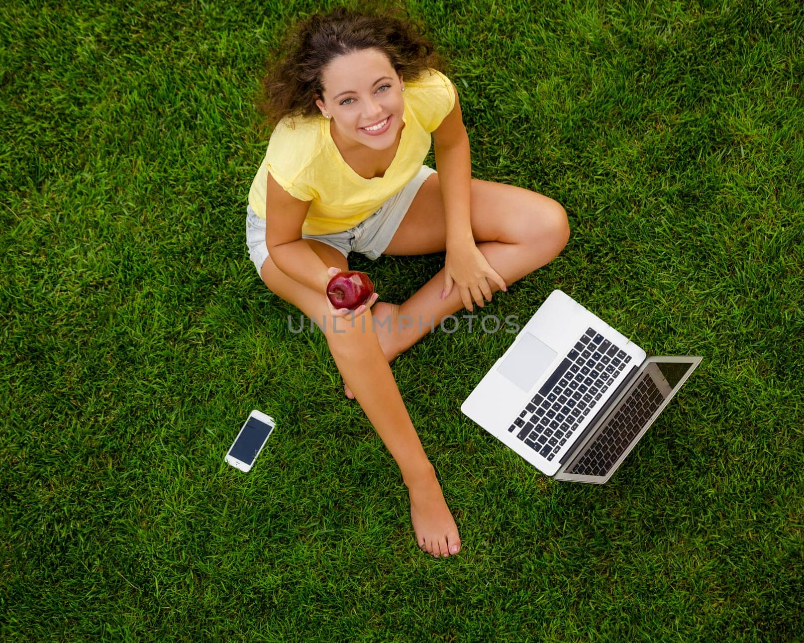 Beautiful young woman lying on the grass and working with a laptop