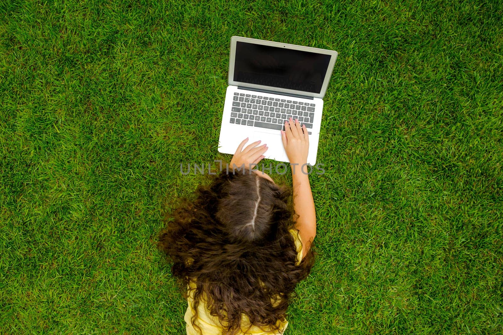 Beautiful young woman lying on the grass and working with a laptop