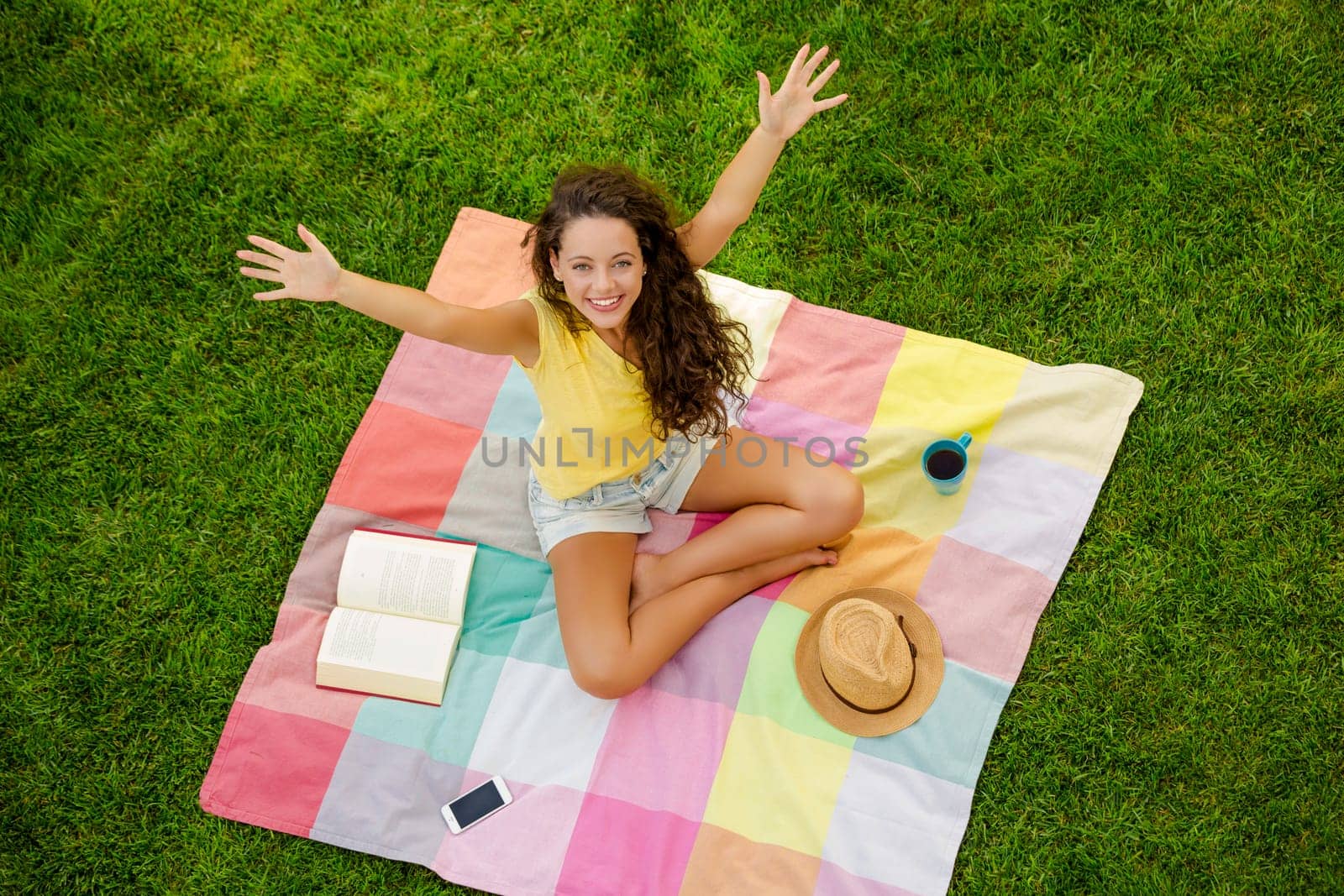 Happy young woman sitting on a blanket with arms stretched