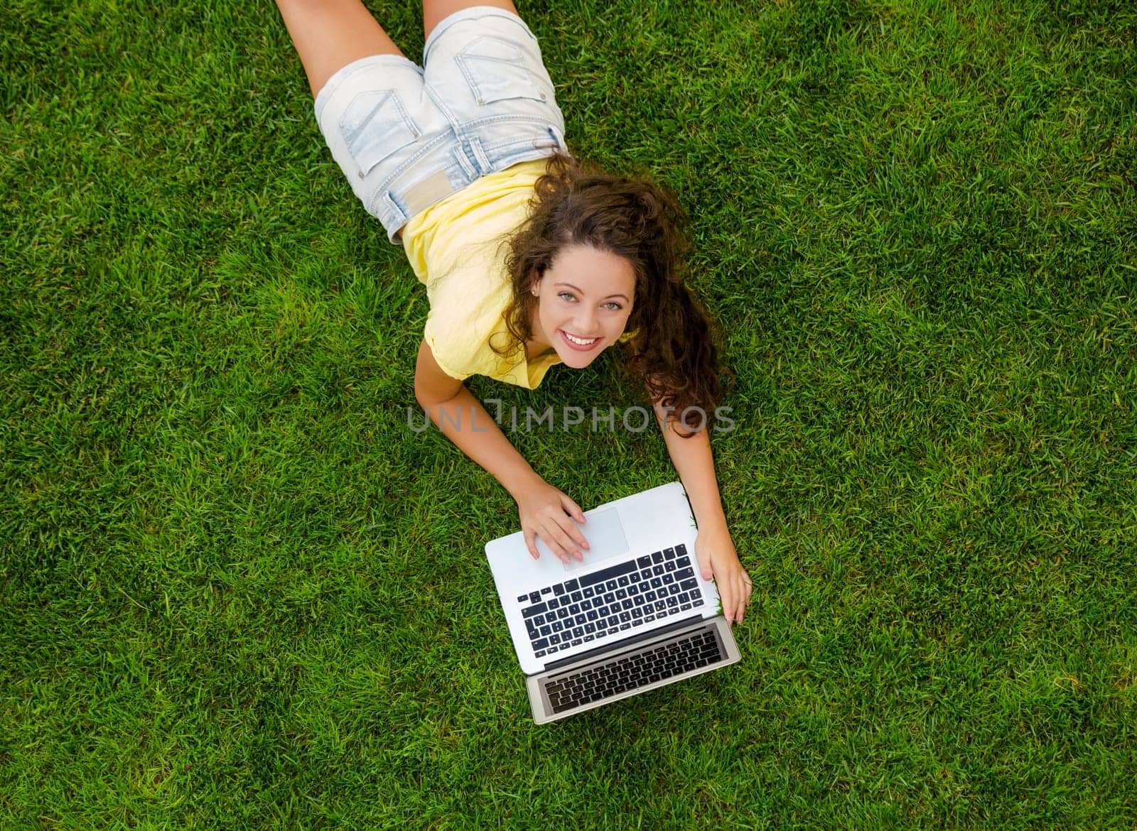 Beautiful young woman lying on the grass and working with a laptop