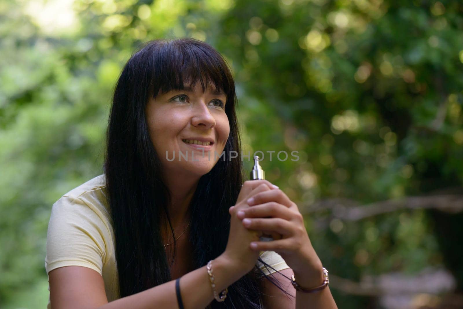 Nice girl smiling and smocking an electronic cigarette in the wood