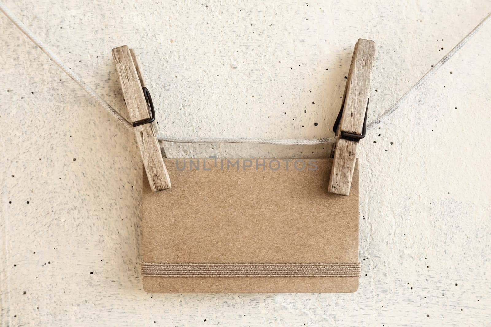 Clothespins holding on clothesline or rope holding brown blank craft paper card on plaster background