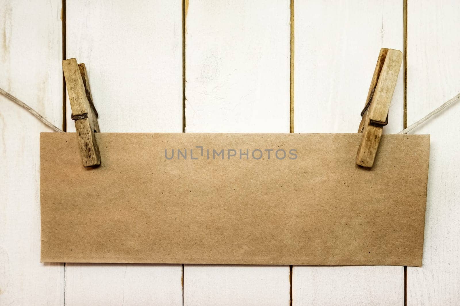 Clothespins holding on clothesline or rope holding brown blank craft paper card on wooden background