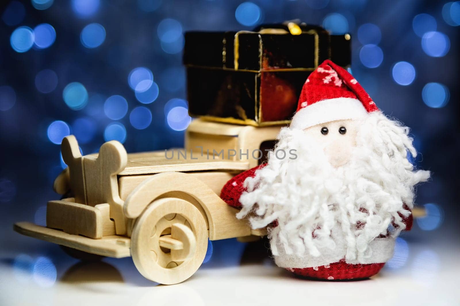 Santa Claus and old vintage wooden automobile with gift box on christmas lights background. Main focus of image on Santa Claus and selective on turned left wood car with gift box