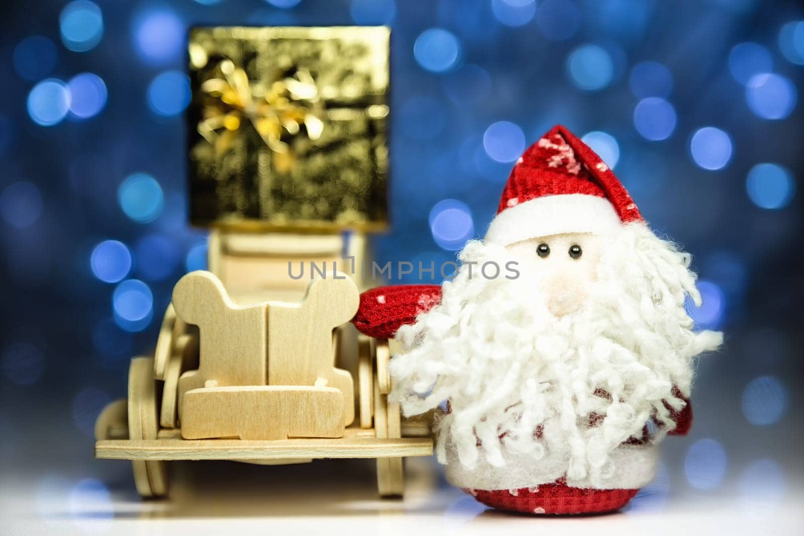 Santa Claus and old vintage wooden automobile with gift box on christmas lights background. Main focus of image on Santa Claus and selective on face standing wood car with gift box