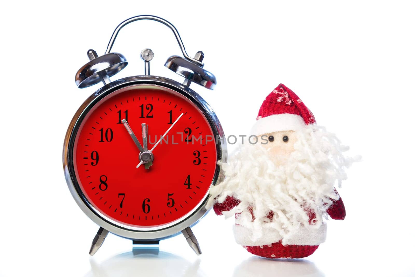 Santa Claus or Father Frost and vintage alarm clock with red dial on white background with reflection. Showing time five minutes before twelve midnight