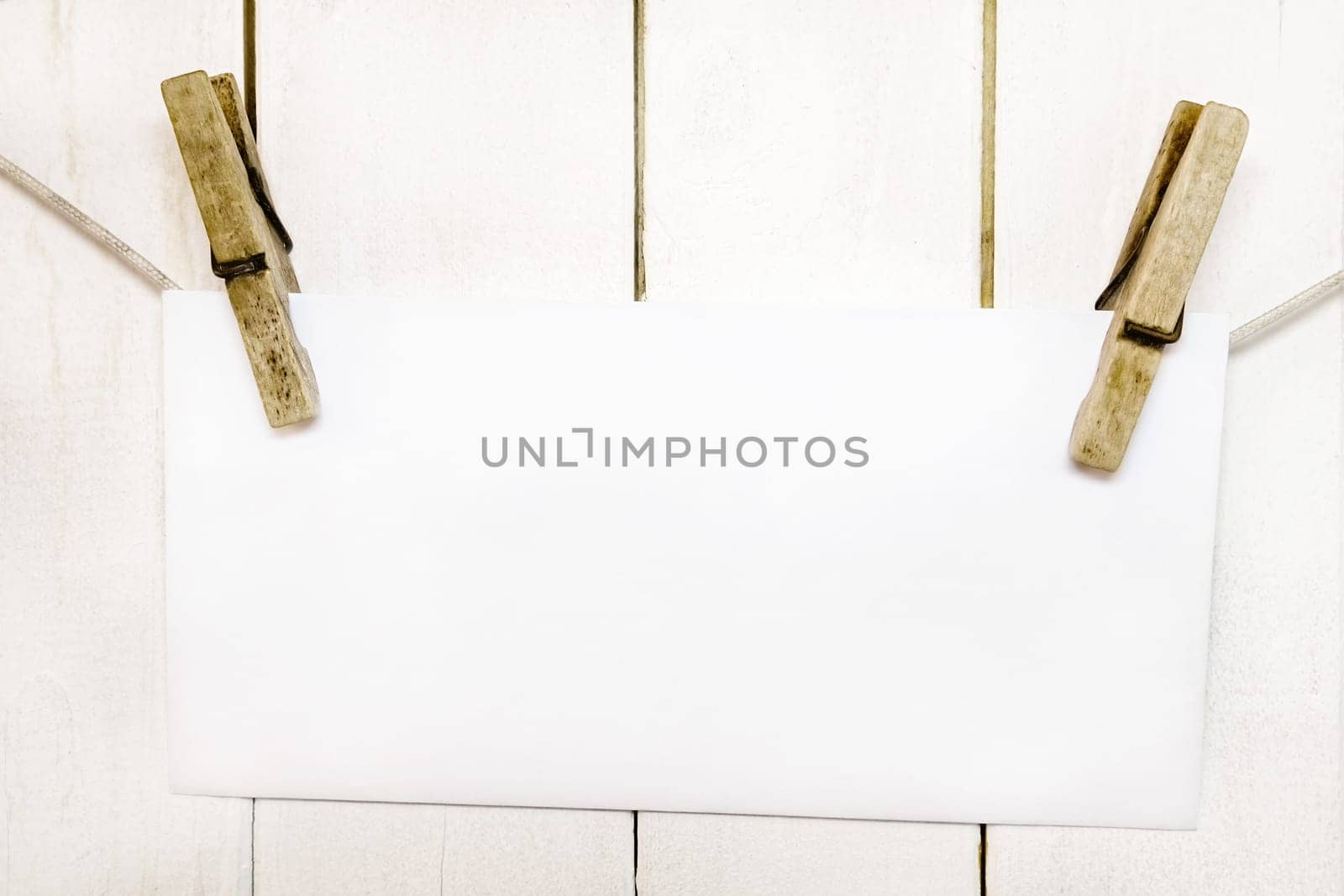 Clothespins holding on clothesline or rope holding white blank paper card on wooden background