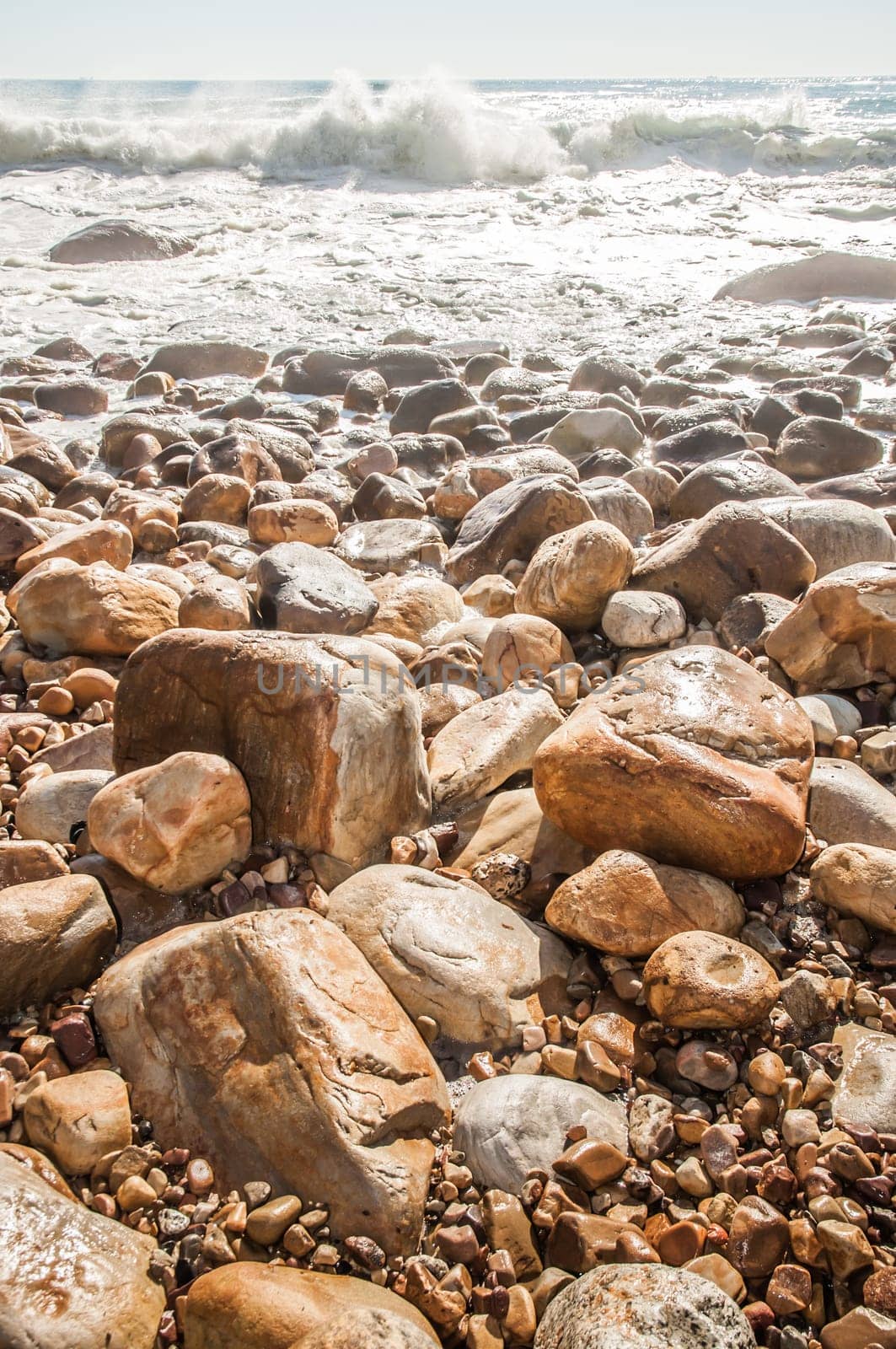 Waves crashing on a rocky beach as the tide is coming in, leaving white wake behind as the water resides.